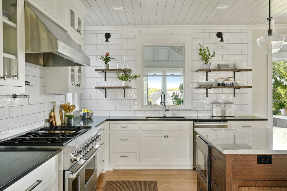 Exempel på ett maritimt kök, med en undermonterad diskho, släta luckor, vita skåp, bänkskiva i kvartsit, stänkskydd i tunnelbanekakel, rostfria vitvaror, ljust trägolv och en köksö