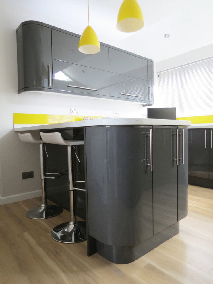 This is an example of a contemporary u-shaped kitchen/diner in Sussex with a submerged sink, grey cabinets, composite countertops, yellow splashback, glass sheet splashback, stainless steel appliances and a breakfast bar.
