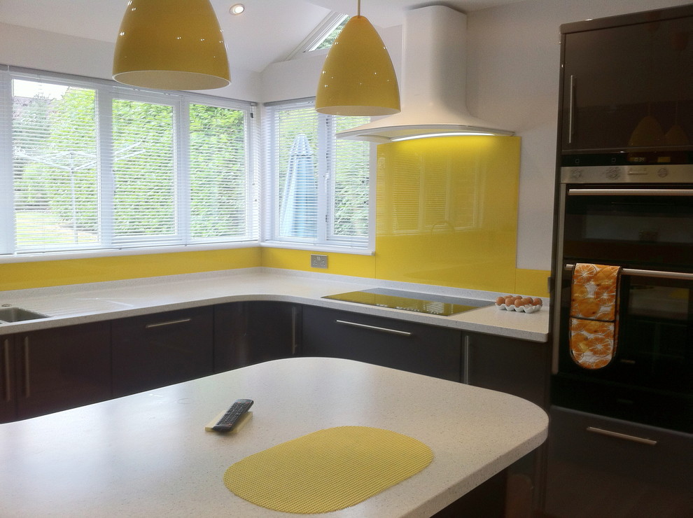 Esempio di una cucina minimal con lavello sottopiano, ante grigie, top in superficie solida, paraspruzzi giallo, paraspruzzi con lastra di vetro, elettrodomestici in acciaio inossidabile e penisola