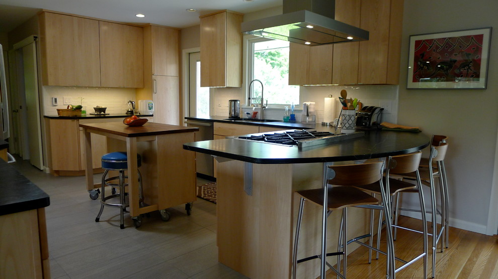 Photo of a modern kitchen/diner in New York with a submerged sink, flat-panel cabinets, light wood cabinets, soapstone worktops, beige splashback, ceramic splashback, stainless steel appliances, porcelain flooring and an island.