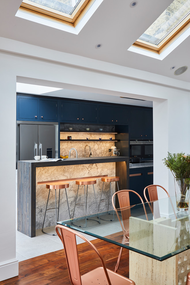 Inspiration for a large contemporary single-wall kitchen pantry in London with a built-in sink, flat-panel cabinets, blue cabinets, granite worktops, grey splashback, marble splashback, stainless steel appliances, ceramic flooring, an island, grey floors and grey worktops.