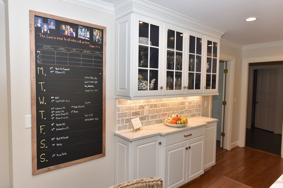 Photo of a large traditional galley kitchen/diner in Cincinnati with a submerged sink, raised-panel cabinets, engineered stone countertops, grey splashback, mosaic tiled splashback, stainless steel appliances, dark hardwood flooring, an island and white cabinets.