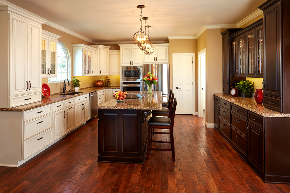 Exempel på ett stort klassiskt kök, med en undermonterad diskho, luckor med upphöjd panel, vita skåp, granitbänkskiva, gult stänkskydd, rostfria vitvaror, mörkt trägolv, en köksö och brunt golv