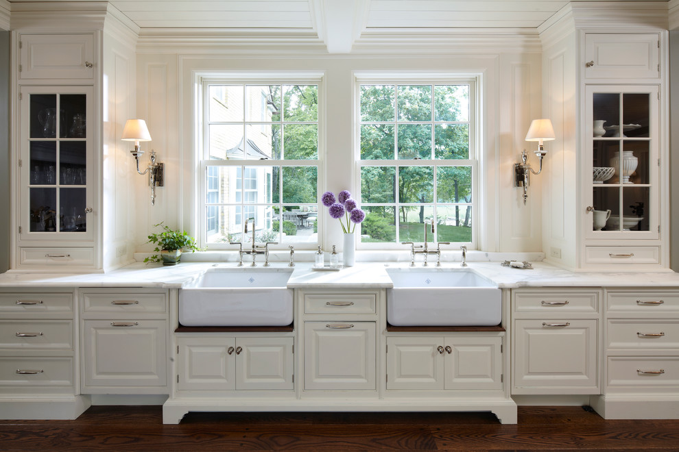 Elegant kitchen photo in Minneapolis with a farmhouse sink, glass-front cabinets, white cabinets and marble countertops