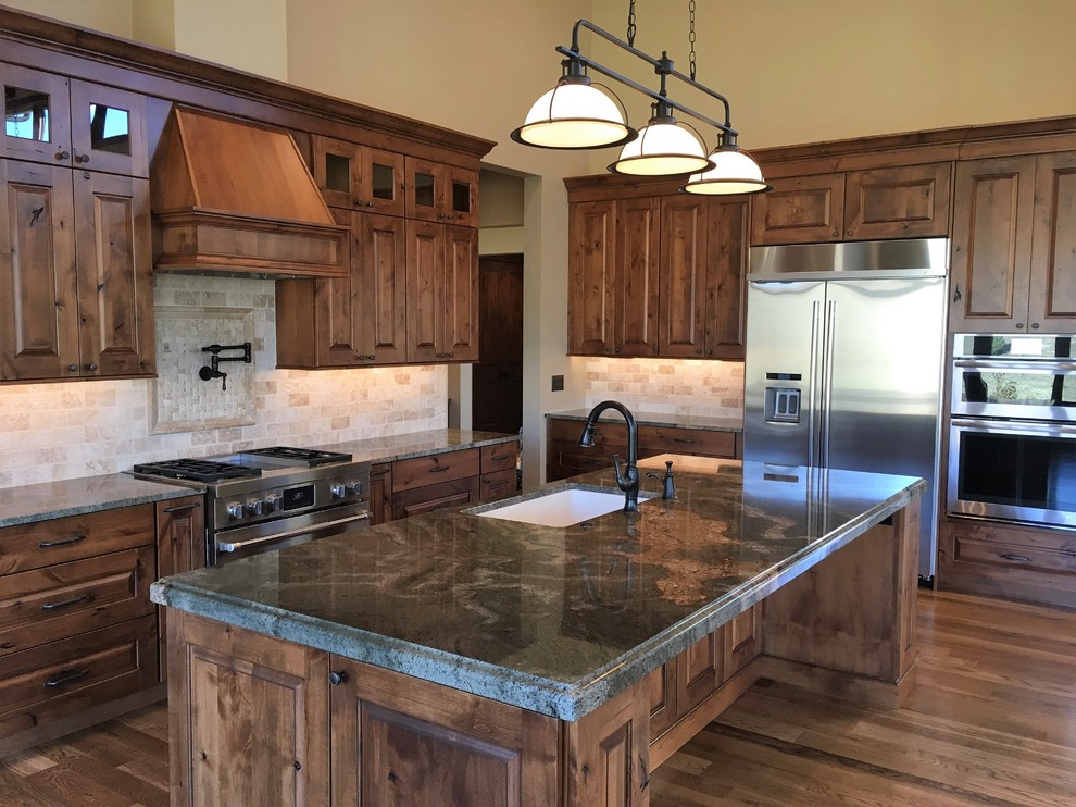 Inspiration for a large rustic l-shaped medium tone wood floor kitchen remodel in Denver with an undermount sink, raised-panel cabinets, brown cabinets, granite countertops, beige backsplash, terra-cotta backsplash, stainless steel appliances and an island