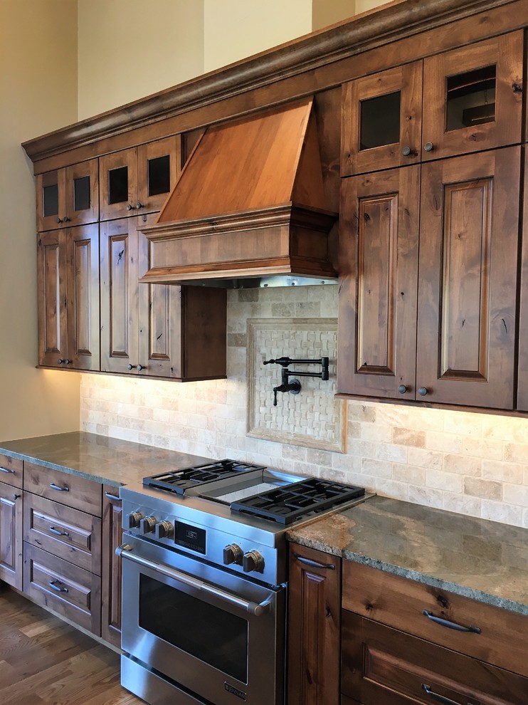 Example of a large mountain style l-shaped medium tone wood floor kitchen design in Denver with an undermount sink, raised-panel cabinets, brown cabinets, granite countertops, beige backsplash, terra-cotta backsplash, stainless steel appliances and an island