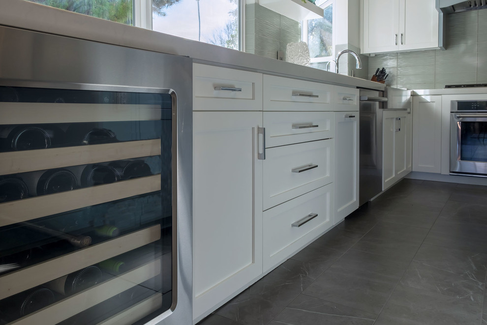 Large classic u-shaped kitchen/diner in Los Angeles with a belfast sink, shaker cabinets, white cabinets, engineered stone countertops, green splashback, glass tiled splashback, stainless steel appliances, porcelain flooring, an island, grey floors and white worktops.