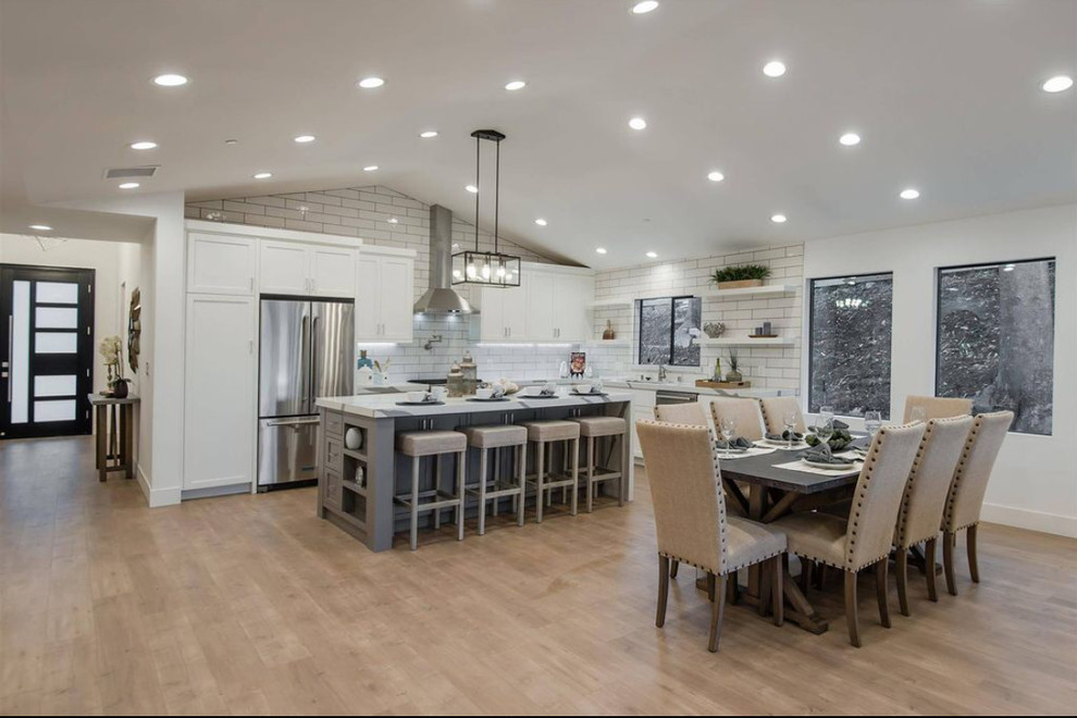 Inspiration for a mid-sized modern l-shaped light wood floor and brown floor open concept kitchen remodel in Los Angeles with an undermount sink, shaker cabinets, white cabinets, quartz countertops, white backsplash, subway tile backsplash, stainless steel appliances, an island and white countertops
