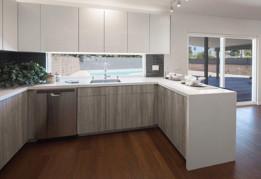Example of a mid-sized trendy u-shaped dark wood floor and brown floor eat-in kitchen design in Los Angeles with an undermount sink, flat-panel cabinets, white cabinets, quartz countertops, gray backsplash, porcelain backsplash, stainless steel appliances and a peninsula