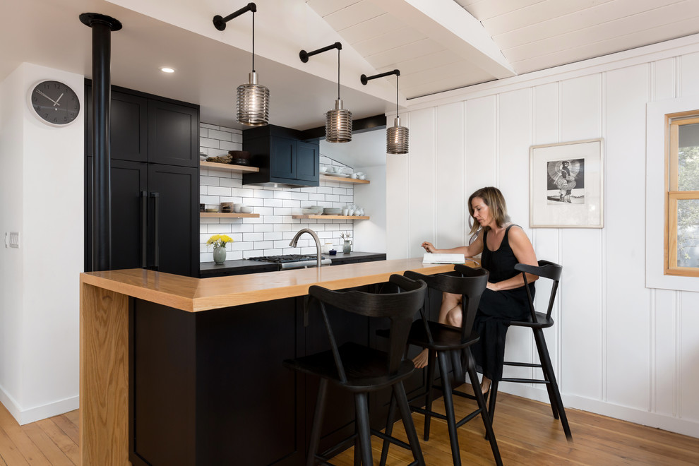 Minimalistisk inredning av ett mellanstort kök, med en undermonterad diskho, skåp i shakerstil, svarta skåp, granitbänkskiva, vitt stänkskydd, stänkskydd i keramik, svarta vitvaror, mellanmörkt trägolv, en halv köksö och orange golv