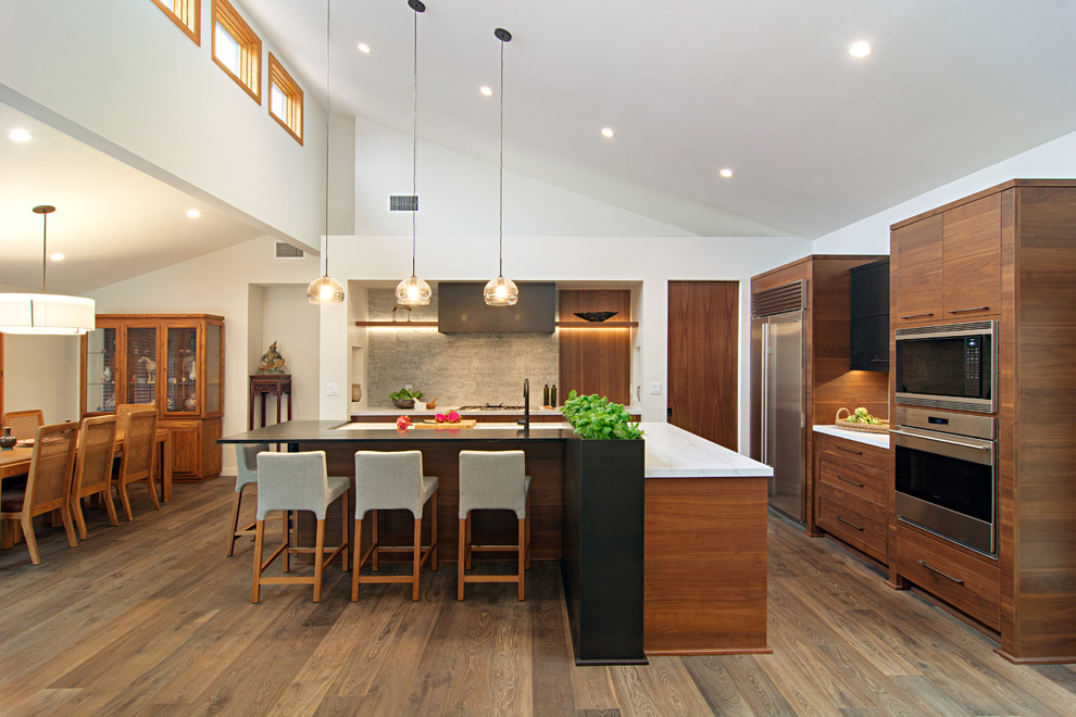 Moderne Küche in L-Form mit flächenbündigen Schrankfronten, hellbraunen Holzschränken, Küchengeräten aus Edelstahl, dunklem Holzboden, Kücheninsel, braunem Boden und weißer Arbeitsplatte in San Diego