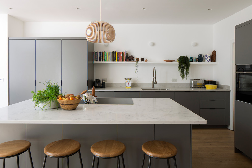 Moderne Küche mit flächenbündigen Schrankfronten, grauen Schränken, Marmor-Arbeitsplatte, hellem Holzboden, Kücheninsel, weißer Arbeitsplatte und Unterbauwaschbecken in London
