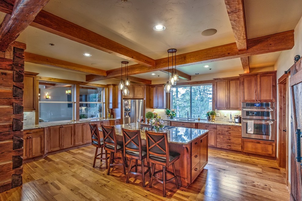 Enclosed kitchen - large rustic l-shaped dark wood floor and brown floor enclosed kitchen idea in Portland with an undermount sink, recessed-panel cabinets, dark wood cabinets, granite countertops, gray backsplash, stone tile backsplash, stainless steel appliances and an island