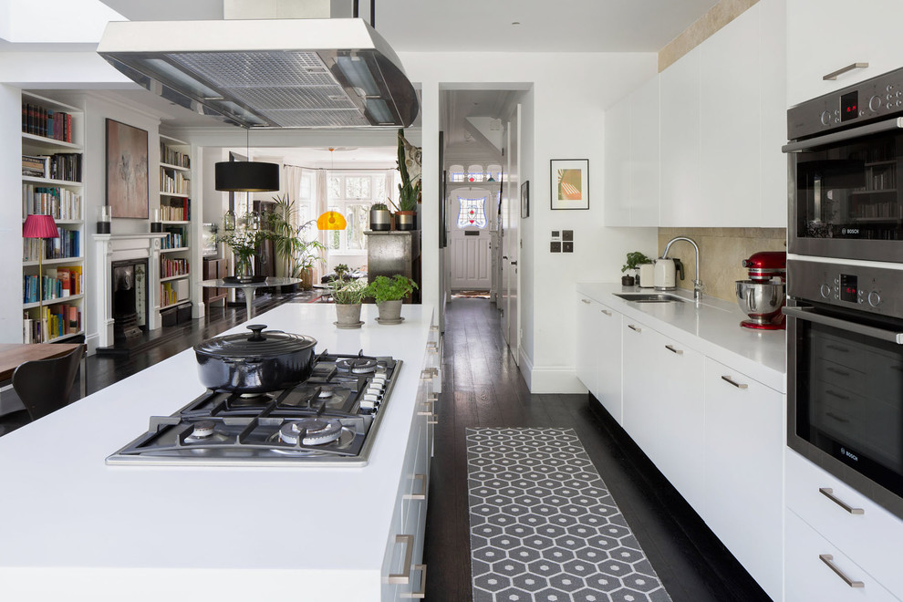 Inredning av ett modernt linjärt kök med öppen planlösning, med en undermonterad diskho, släta luckor, vita skåp, mörkt trägolv, en köksö och brunt golv