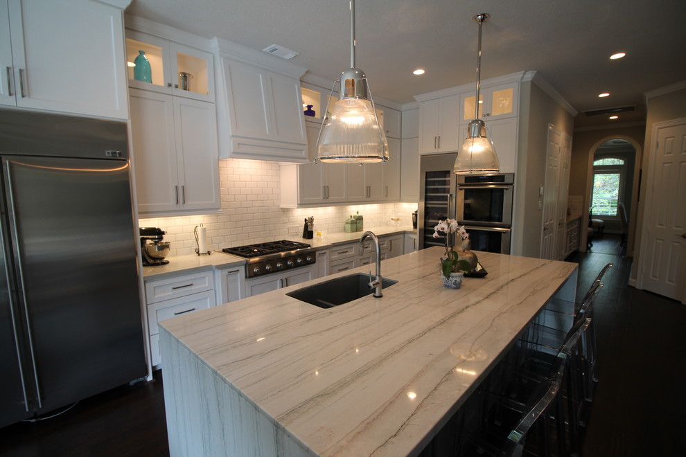 This is an example of a large classic l-shaped kitchen in Houston with a double-bowl sink, shaker cabinets, white cabinets, marble worktops, white splashback, metro tiled splashback, stainless steel appliances, dark hardwood flooring and an island.