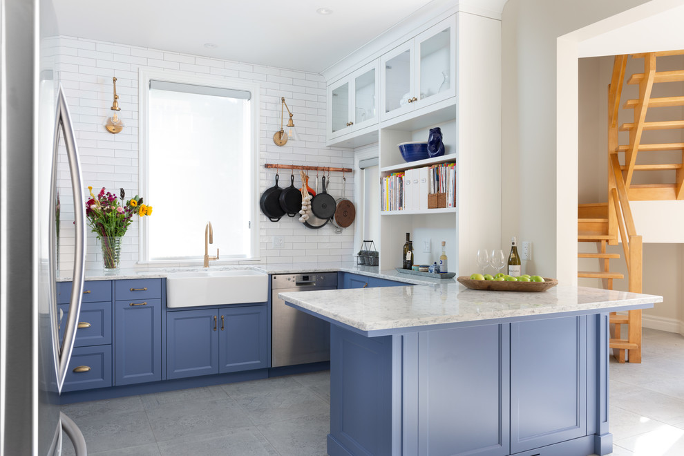 This is an example of a medium sized traditional u-shaped kitchen pantry in Ottawa with a belfast sink, shaker cabinets, blue cabinets, engineered stone countertops, white splashback, ceramic splashback, stainless steel appliances, porcelain flooring, a breakfast bar, grey floors and grey worktops.