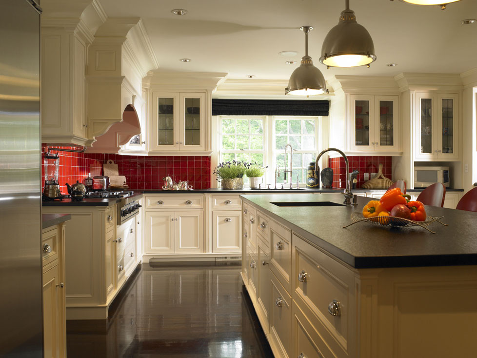 Klassisk inredning av ett stort kök, med en undermonterad diskho, luckor med infälld panel, vita skåp, granitbänkskiva, rött stänkskydd, stänkskydd i keramik, rostfria vitvaror, mörkt trägolv och en köksö