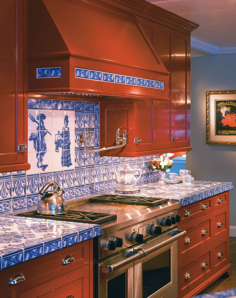 This is an example of a large classic kitchen/diner in Boston with stainless steel appliances, tile countertops, recessed-panel cabinets, red cabinets, blue splashback, a belfast sink, ceramic splashback, dark hardwood flooring and an island.