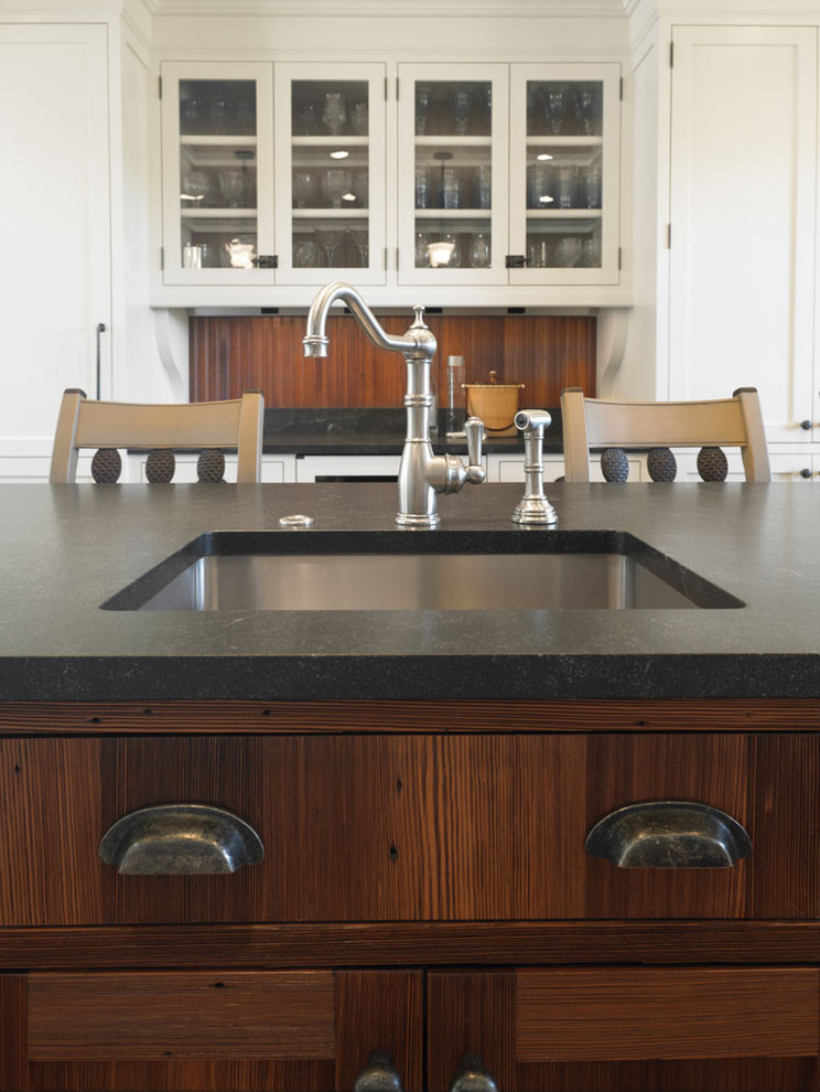 Example of a large classic medium tone wood floor kitchen design in Boston with a farmhouse sink, recessed-panel cabinets, distressed cabinets, granite countertops, white backsplash, ceramic backsplash, paneled appliances and an island