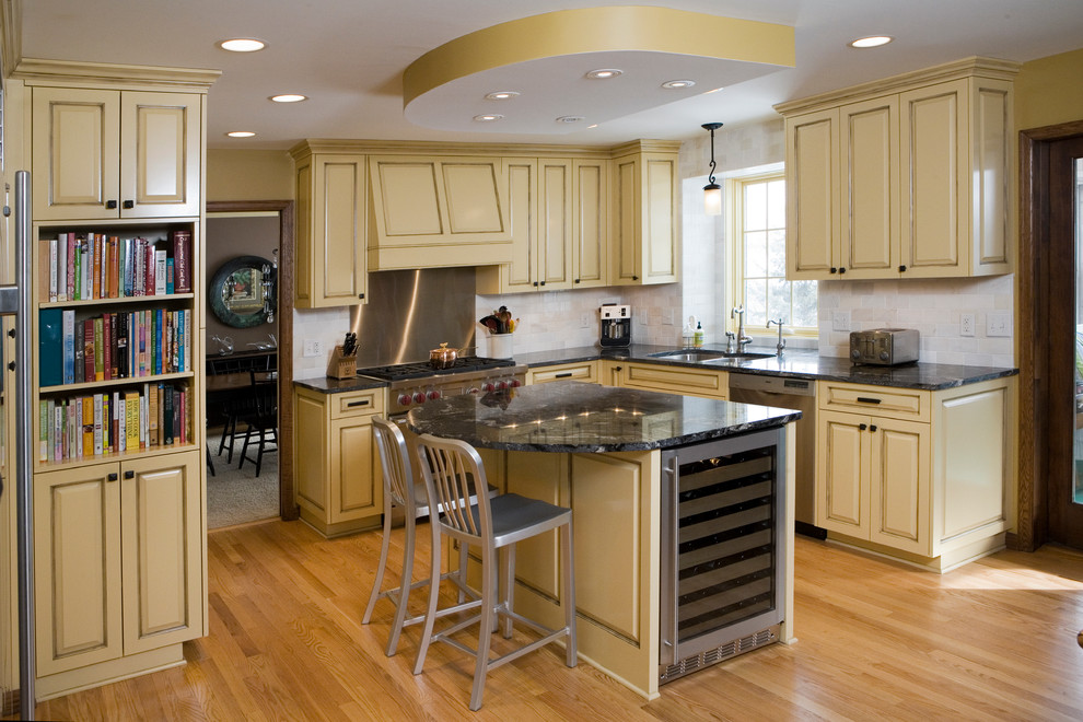 Klassische Wohnküche mit Unterbauwaschbecken, profilierten Schrankfronten, gelben Schränken, Kalkstein-Arbeitsplatte und Küchengeräten aus Edelstahl in Minneapolis