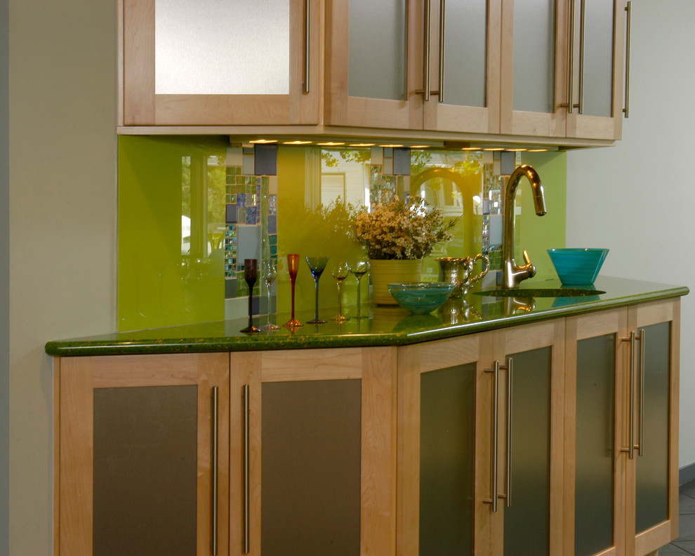 Inspiration for a medium sized eclectic l-shaped home bar in New York with flat-panel cabinets, light wood cabinets, green splashback, glass tiled splashback, a submerged sink, engineered stone countertops and ceramic flooring.
