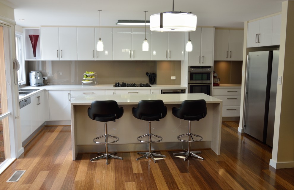 Große Moderne Wohnküche in L-Form mit Doppelwaschbecken, offenen Schränken, weißen Schränken, Granit-Arbeitsplatte, Küchenrückwand in Braun, Glasrückwand, Küchengeräten aus Edelstahl, Bambusparkett und Kücheninsel in Melbourne