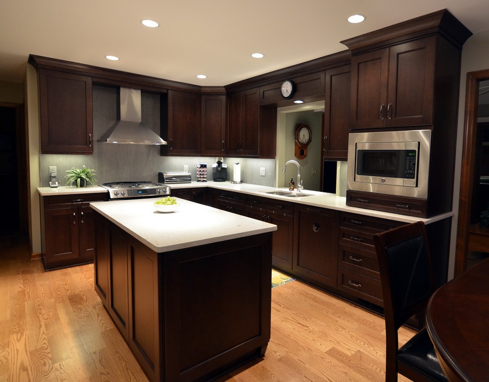Inspiration for a mid-sized transitional l-shaped medium tone wood floor enclosed kitchen remodel in Other with an undermount sink, recessed-panel cabinets, dark wood cabinets, quartz countertops, gray backsplash, porcelain backsplash, stainless steel appliances and an island