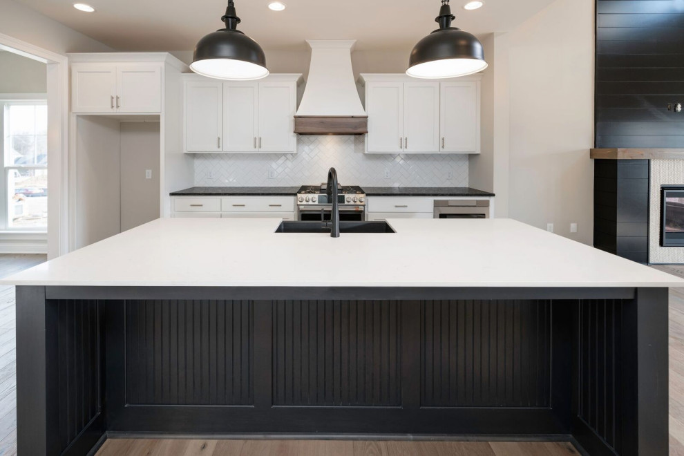 Urban single-wall medium tone wood floor and brown floor open concept kitchen photo in Huntington with a farmhouse sink, recessed-panel cabinets, black cabinets, quartz countertops, white backsplash, ceramic backsplash, stainless steel appliances, an island and white countertops