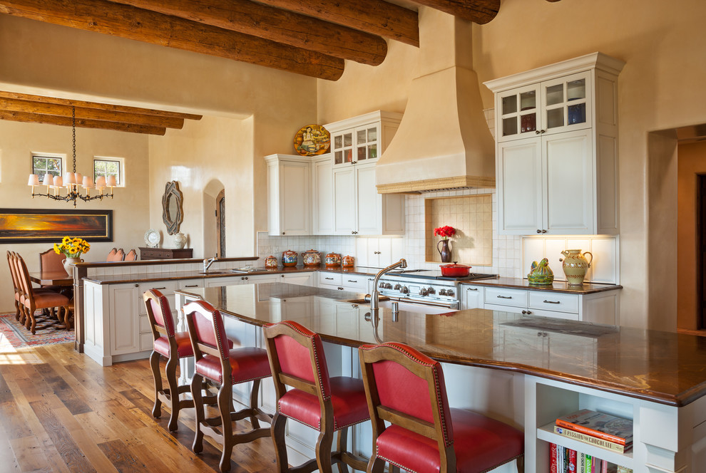 Mediterrane Wohnküche mit Schrankfronten mit vertiefter Füllung, weißen Schränken, Küchenrückwand in Weiß, Küchengeräten aus Edelstahl, braunem Holzboden und Kücheninsel in Albuquerque