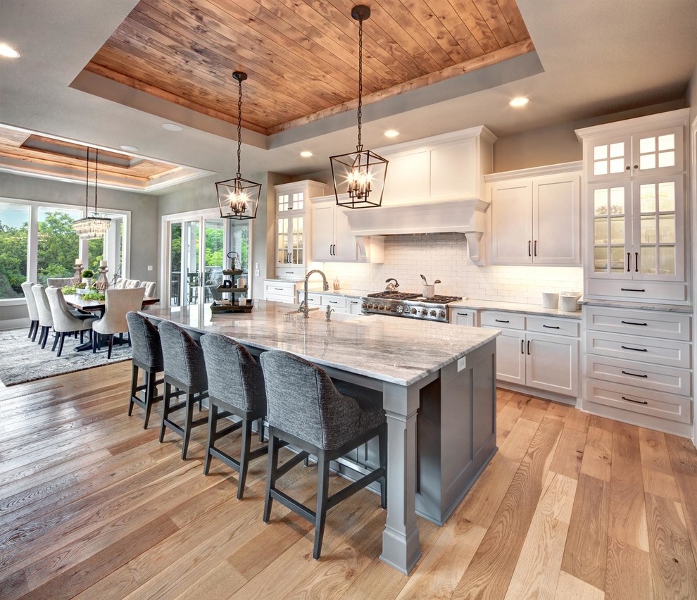 Example of a classic light wood floor and beige floor eat-in kitchen design in Kansas City with a farmhouse sink, white cabinets, white backsplash, subway tile backsplash, stainless steel appliances, an island, gray countertops and shaker cabinets