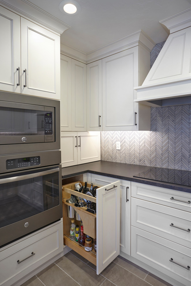 Klassisk inredning av ett mellanstort svart svart kök, med en undermonterad diskho, luckor med infälld panel, vita skåp, granitbänkskiva, grått stänkskydd, stänkskydd i glaskakel, rostfria vitvaror, klinkergolv i porslin, en halv köksö och beiget golv