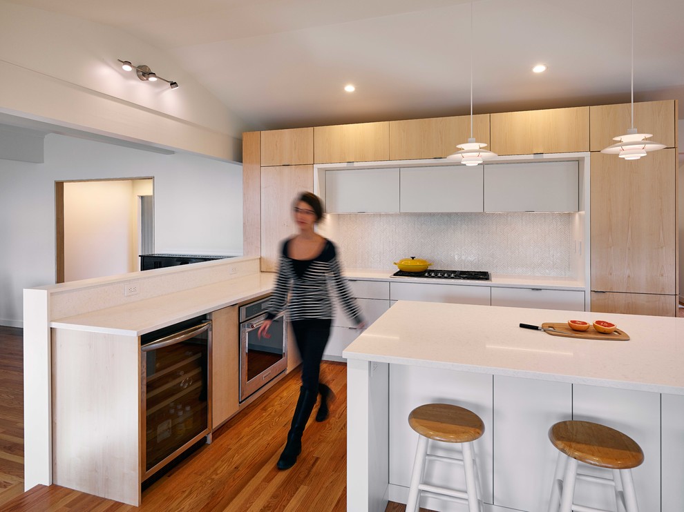 Inspiration for a medium sized retro l-shaped kitchen in Baltimore with flat-panel cabinets, light wood cabinets, composite countertops, white splashback, ceramic splashback, stainless steel appliances, an island, white worktops and medium hardwood flooring.