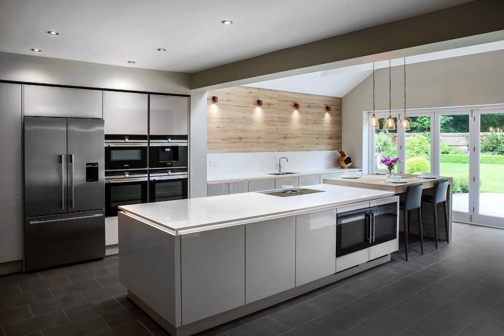 Exempel på ett stort modernt vit linjärt vitt kök med öppen planlösning, med en integrerad diskho, släta luckor, grå skåp, bänkskiva i kvartsit, vitt stänkskydd, stänkskydd i sten, integrerade vitvaror, laminatgolv, en köksö och grått golv