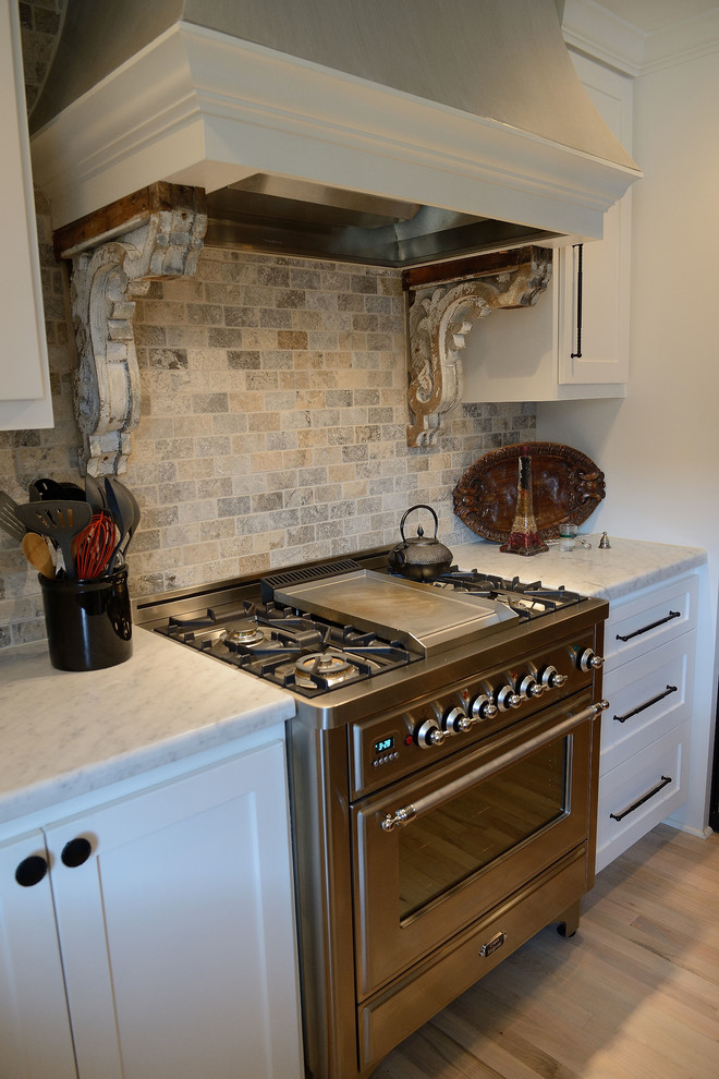 Lantlig inredning av ett mellanstort kök, med skåp i shakerstil, vita skåp, marmorbänkskiva, grått stänkskydd, stänkskydd i stenkakel, rostfria vitvaror och ljust trägolv