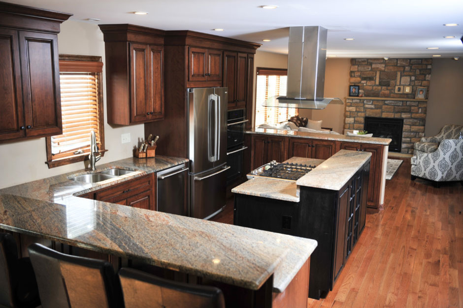 Photo of a medium sized traditional u-shaped kitchen/diner in Philadelphia with a double-bowl sink, raised-panel cabinets, dark wood cabinets, granite worktops, stainless steel appliances, light hardwood flooring and multiple islands.