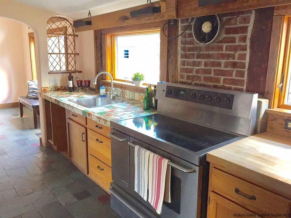 Foto på ett mellanstort amerikanskt kök, med en nedsänkt diskho, skåp i shakerstil, skåp i ljust trä, träbänkskiva, brunt stänkskydd, stänkskydd i tegel, rostfria vitvaror och cementgolv