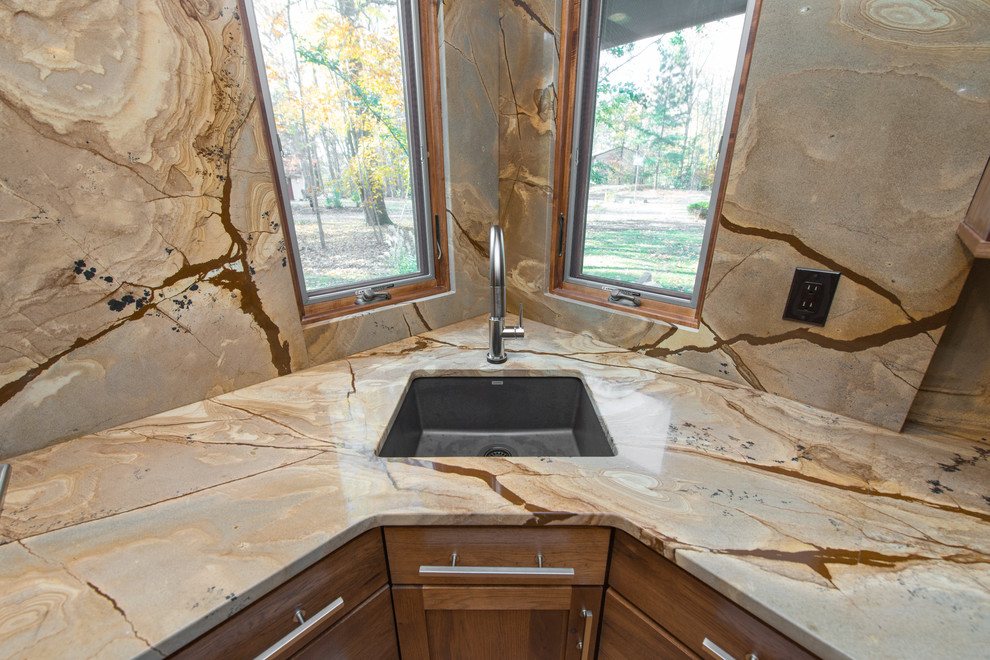 Bild på ett mellanstort funkis kök, med en undermonterad diskho, släta luckor, skåp i mellenmörkt trä, bänkskiva i kvartsit, brunt stänkskydd, stänkskydd i sten, rostfria vitvaror, ljust trägolv och en köksö