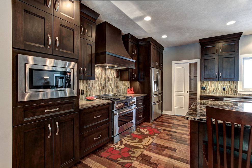 Photo of a traditional l-shaped kitchen/diner in Grand Rapids with an integrated sink, shaker cabinets, dark wood cabinets, composite countertops, brown splashback, glass tiled splashback, stainless steel appliances, medium hardwood flooring and an island.