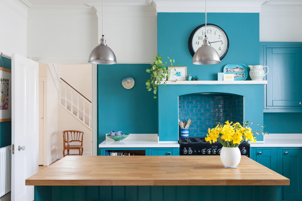 Geschlossene, Mittelgroße Klassische Küche mit Mineralwerkstoff-Arbeitsplatte, schwarzen Elektrogeräten, Kücheninsel, weißer Arbeitsplatte, Schrankfronten im Shaker-Stil, blauen Schränken, Einbauwaschbecken, Küchenrückwand in Weiß und hellem Holzboden in Sussex
