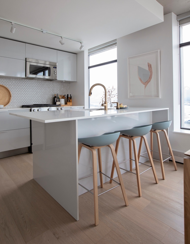 Medium sized contemporary galley kitchen in Vancouver with a submerged sink, flat-panel cabinets, white cabinets, white splashback, light hardwood flooring, an island, beige floors and white worktops.