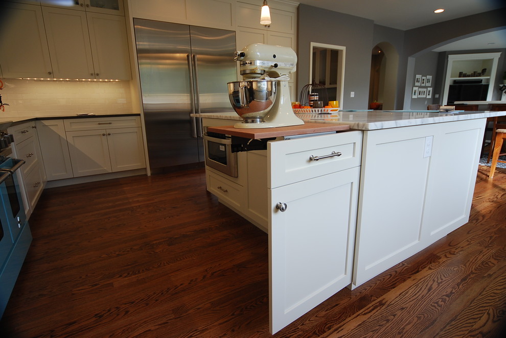 Große Wohnküche in U-Form mit weißen Schränken, Granit-Arbeitsplatte, Küchenrückwand in Weiß, Küchengeräten aus Edelstahl, braunem Holzboden und Kücheninsel in Seattle