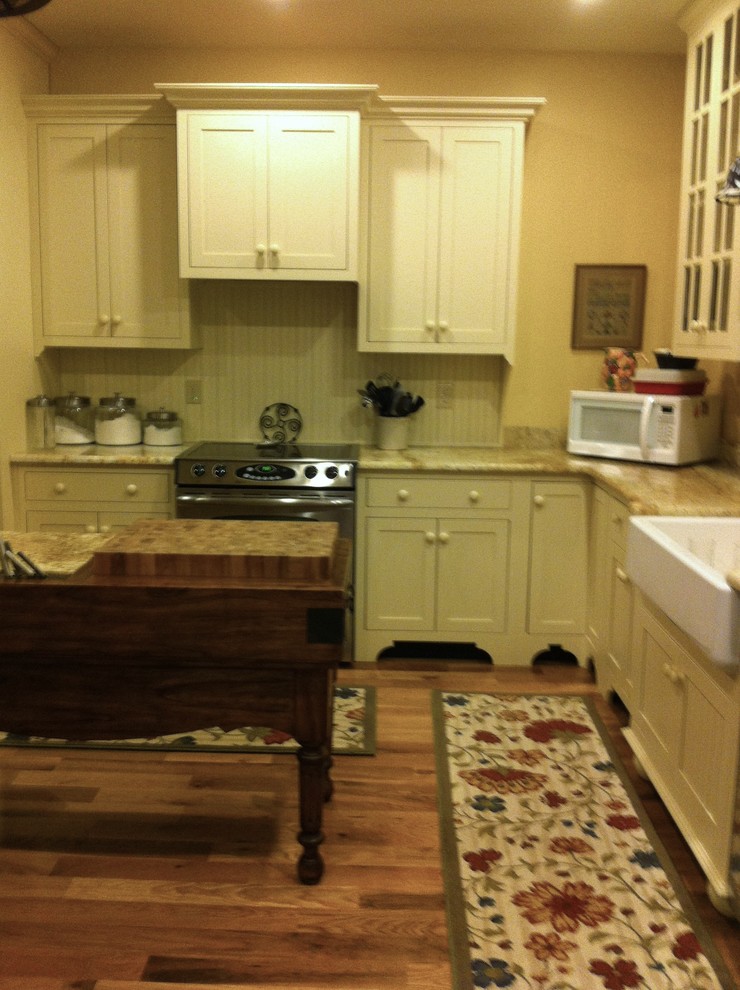 Photo of a medium sized country l-shaped kitchen/diner in Louisville with a belfast sink, flat-panel cabinets, beige cabinets, granite worktops, yellow splashback, stainless steel appliances, medium hardwood flooring and an island.
