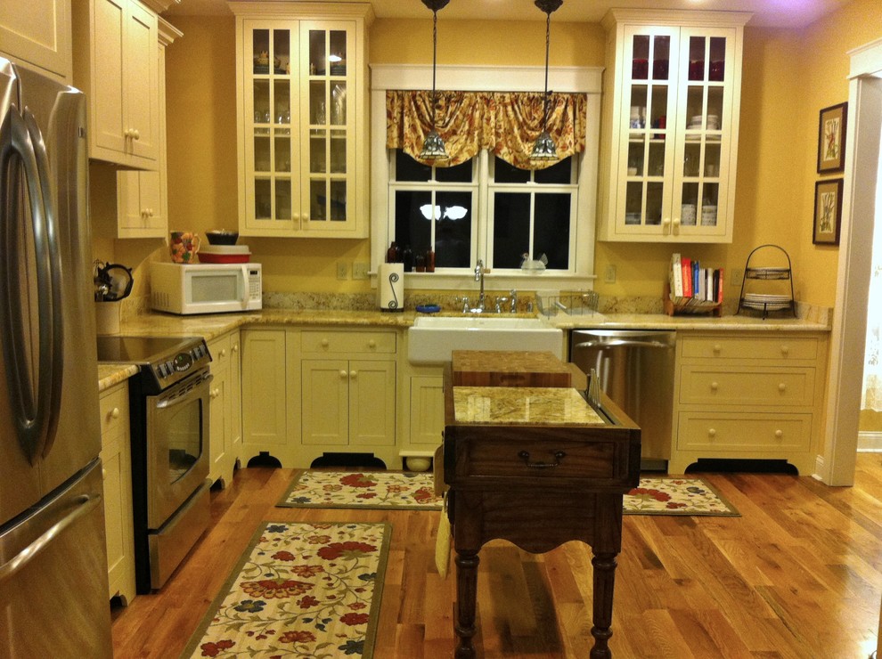 Mittelgroße Country Wohnküche in L-Form mit Landhausspüle, flächenbündigen Schrankfronten, beigen Schränken, Granit-Arbeitsplatte, Küchenrückwand in Gelb, Küchengeräten aus Edelstahl, braunem Holzboden und Kücheninsel in Louisville
