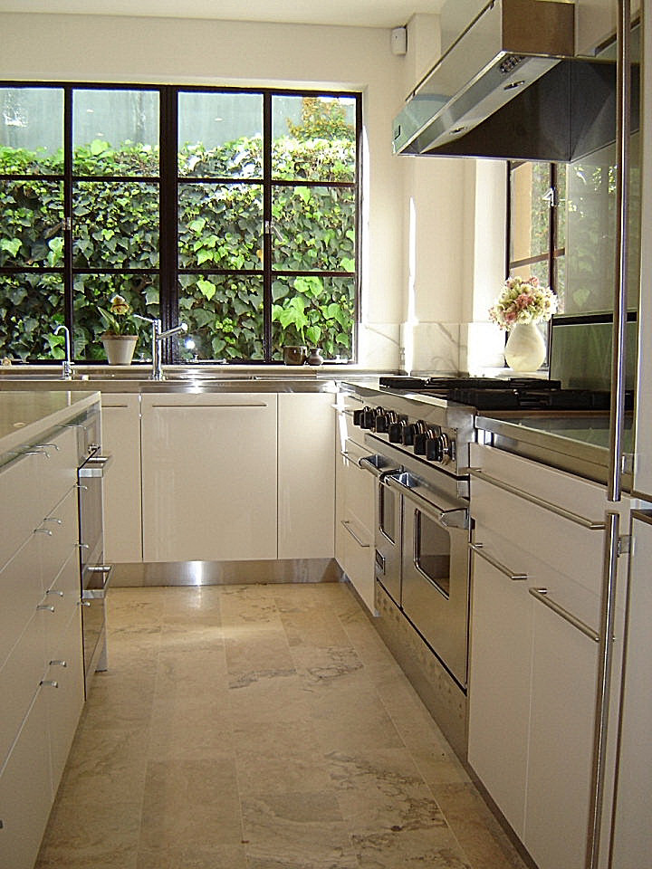 Inspiration för ett mellanstort funkis kök, med en integrerad diskho, släta luckor, vita skåp, marmorbänkskiva, rostfria vitvaror, travertin golv och en köksö