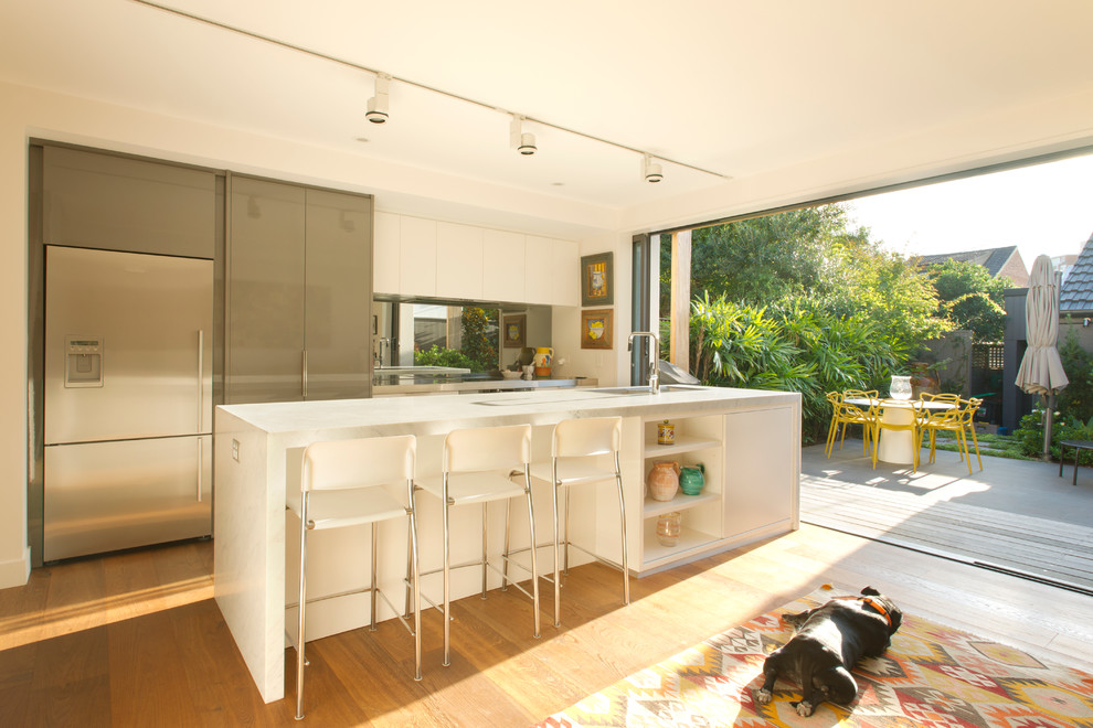 Diseño de cocina comedor contemporánea con armarios con paneles lisos, puertas de armario grises, suelo de madera clara y una isla