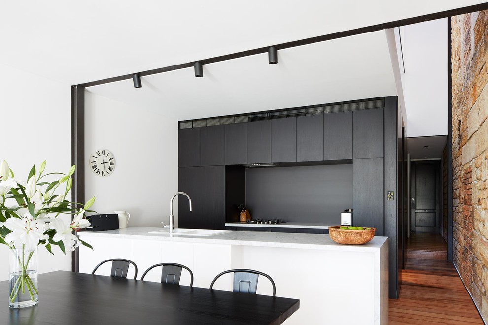 Стильный дизайн: параллельная кухня в стиле модернизм с обеденным столом, двойной мойкой, плоскими фасадами, серым фартуком, паркетным полом среднего тона, полуостровом, красным полом, черно-белыми фасадами и двухцветным гарнитуром - последний тренд