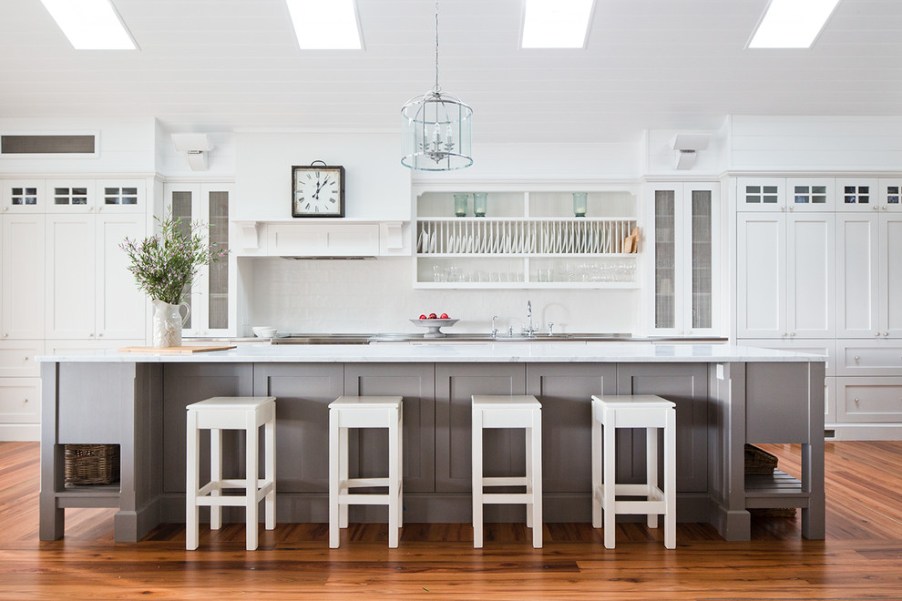 Einzeilige, Große Klassische Küche in grau-weiß mit Schrankfronten im Shaker-Stil, weißen Schränken, Marmor-Arbeitsplatte, Küchenrückwand in Weiß, braunem Holzboden und Kücheninsel in Sydney