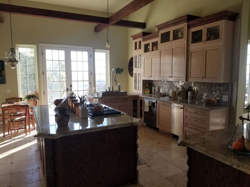 Example of a large ornate l-shaped travertine floor and multicolored floor kitchen pantry design with a farmhouse sink, raised-panel cabinets, dark wood cabinets, granite countertops, multicolored backsplash, stainless steel appliances, two islands and multicolored countertops