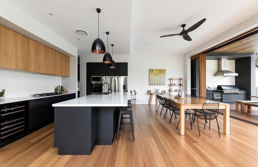 Moderne Wohnküche in U-Form mit flächenbündigen Schrankfronten, schwarzen Schränken, Küchengeräten aus Edelstahl, braunem Holzboden, Kücheninsel, braunem Boden und weißer Arbeitsplatte in Brisbane