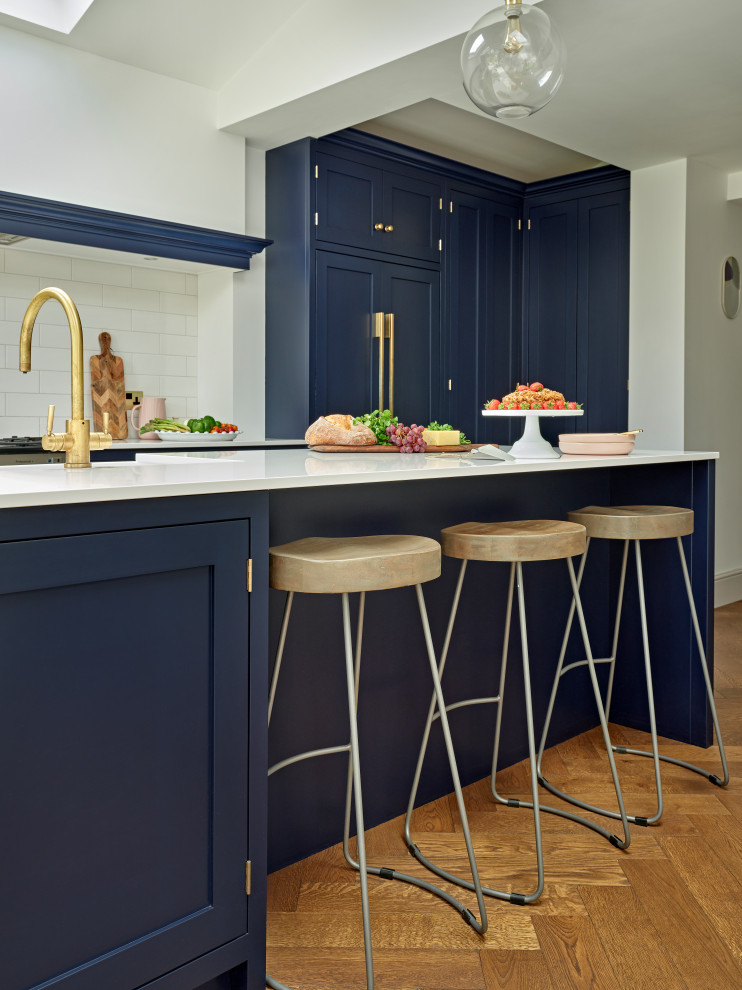 Inspiration for a large classic single-wall kitchen/diner in London with shaker cabinets, an island, a belfast sink, blue cabinets, quartz worktops, white splashback, ceramic splashback, integrated appliances, white worktops and a vaulted ceiling.